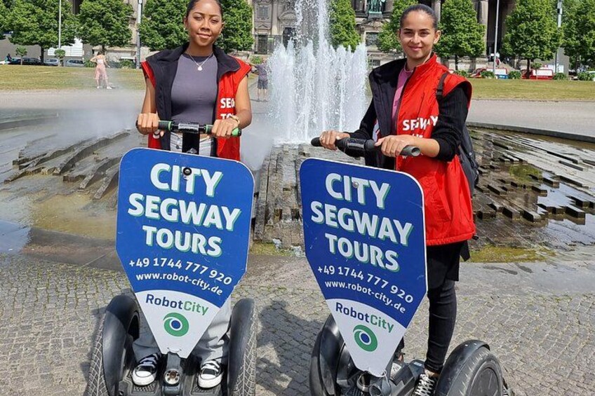 Dos personas en vehículos tipo segway con un cartel de City Segway Tours. 2