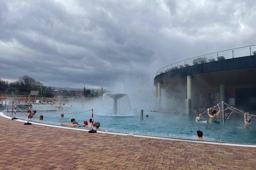 A hot spring pool with people swimming and a waterfall feature. 5