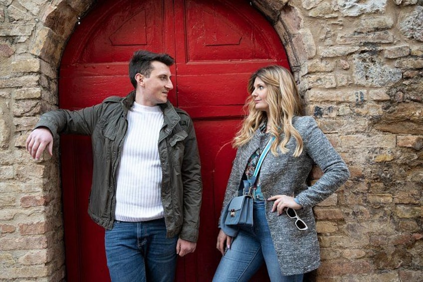 A man and a woman standing in front of a red door with stone walls. 4
