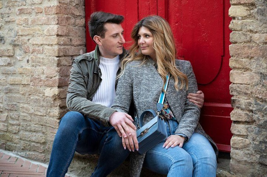 Two people sitting on a brick wall with a red door in the background. 3