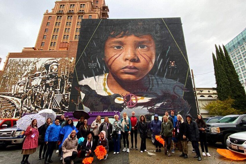 A large mural with a child, a crowd of people, and a cityscape in the background. 1