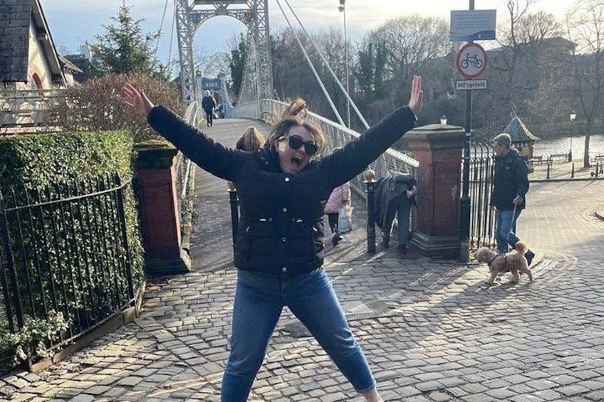 En person står i en park med armarna lyfta, och i bakgrunden syns en bro. 4
