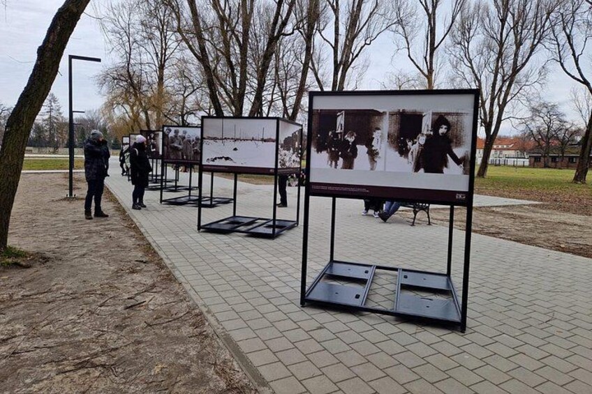 Outdoor display boards with photographs, a paved walkway, and leafless trees. 2