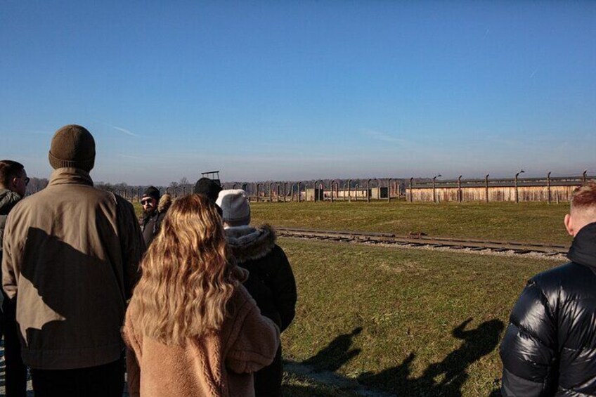 A group of people standing on a grassy area near railway tracks. 4