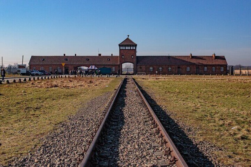 A railway track leading to a large brick building with a tower, surrounded by open fields. 5