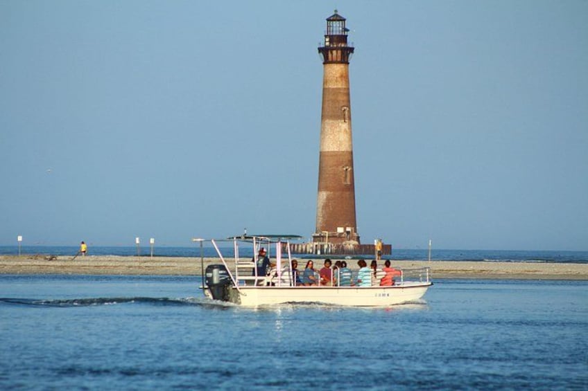 Un bateau avec des personnes à bord, près d’un grand phare de couleur sombre, situé au bord de la côte. 4