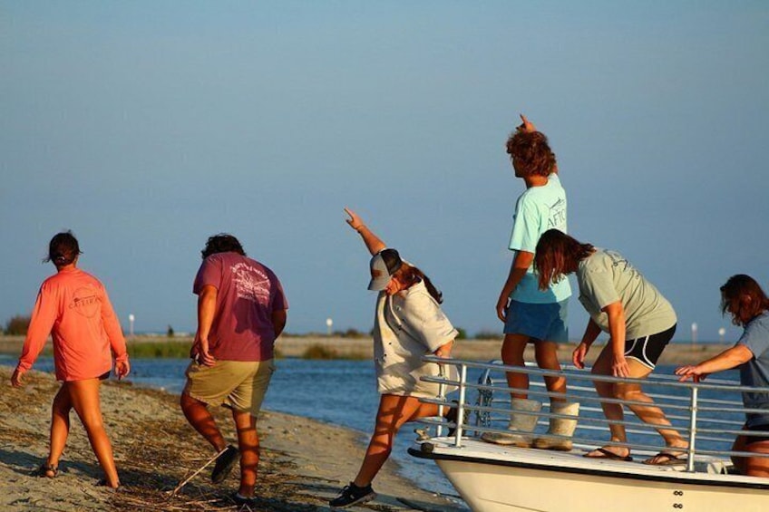 A group of people on a beach, some standing on a boat and others on the shore. 2