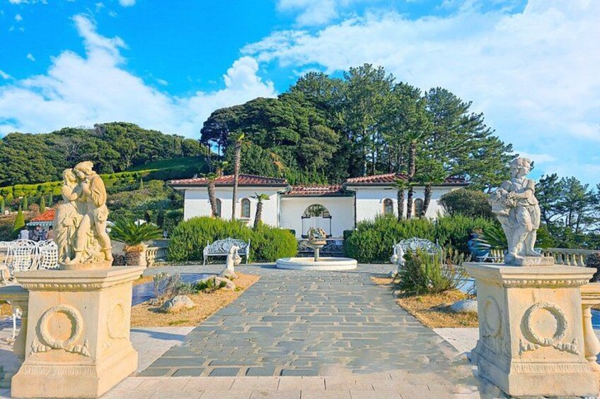 A garden with statues, a pathway, and a building with a red-tiled roof. 5