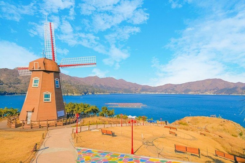 A windmill, a path, benches, and a body of water with mountains in the background. 2