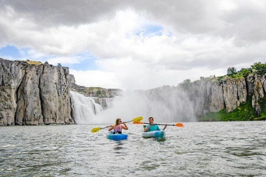 Two people kayaking on a river with a waterfall in the background. 3