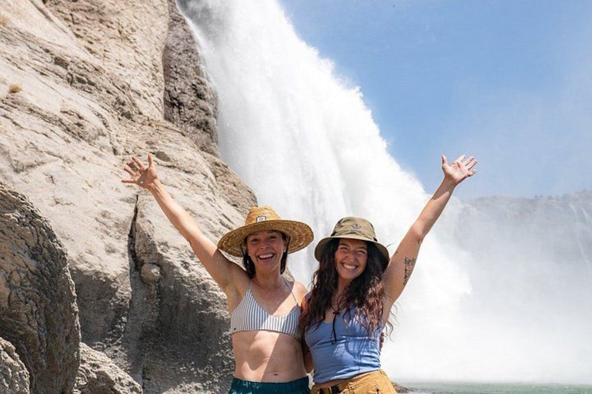 Two people standing in front of a waterfall with their arms raised. 1
