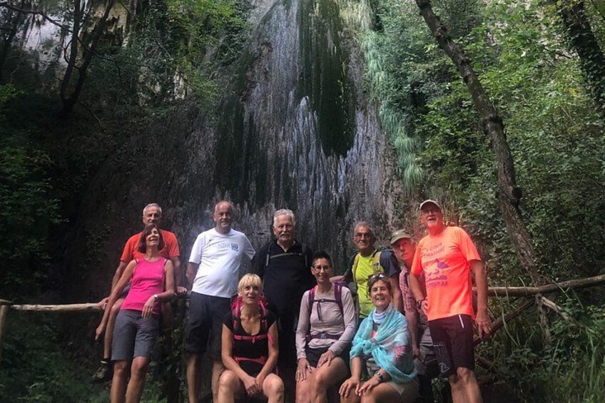 Un groupe de personnes se tient devant une cascade, dans une zone boisée. 2