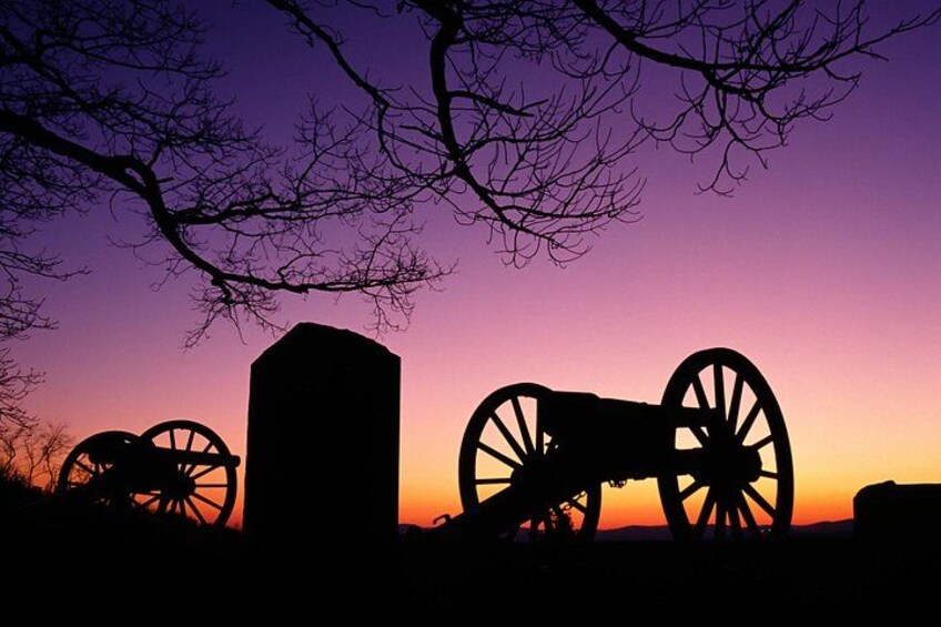 Un coucher de soleil avec la silhouette d’un canon et de deux grandes roues, probablement des éléments d’un site historique. 4