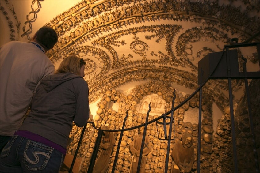 A person standing on a staircase with a wall decorated with skulls and intricate designs. 1