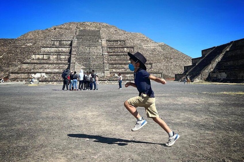 A person running in front of a large pyramid-like structure with a group of people standing in the background. 2