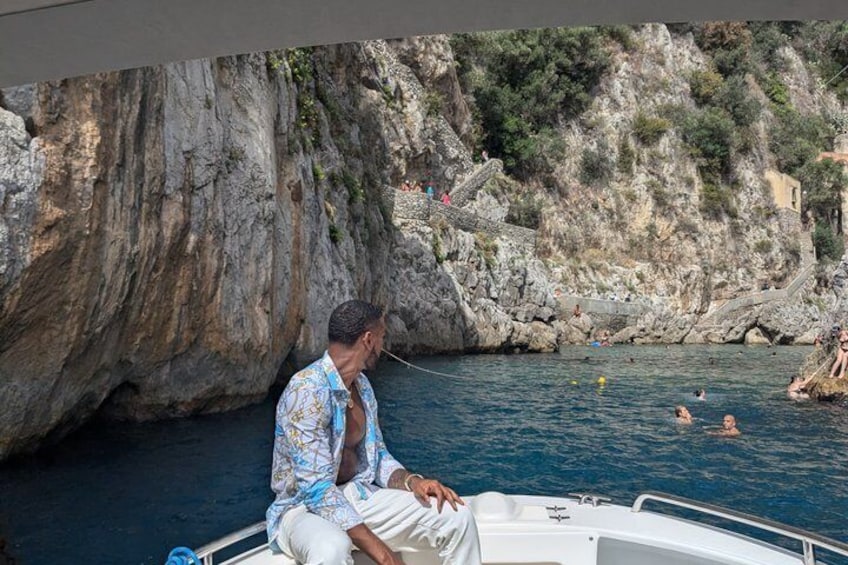 A man on a boat near rocky cliffs with people swimming in the water. 1
