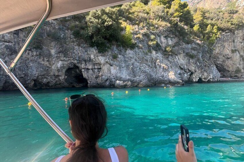 A person on a boat, water, and a rocky cliff with vegetation. 5
