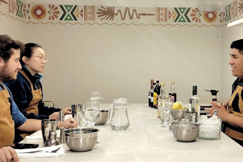 Un grupo de personas sentadas alrededor de una mesa con diversos utensilios de cocina y botellas, probablemente participando en una actividad de cocina o repostería. 5
