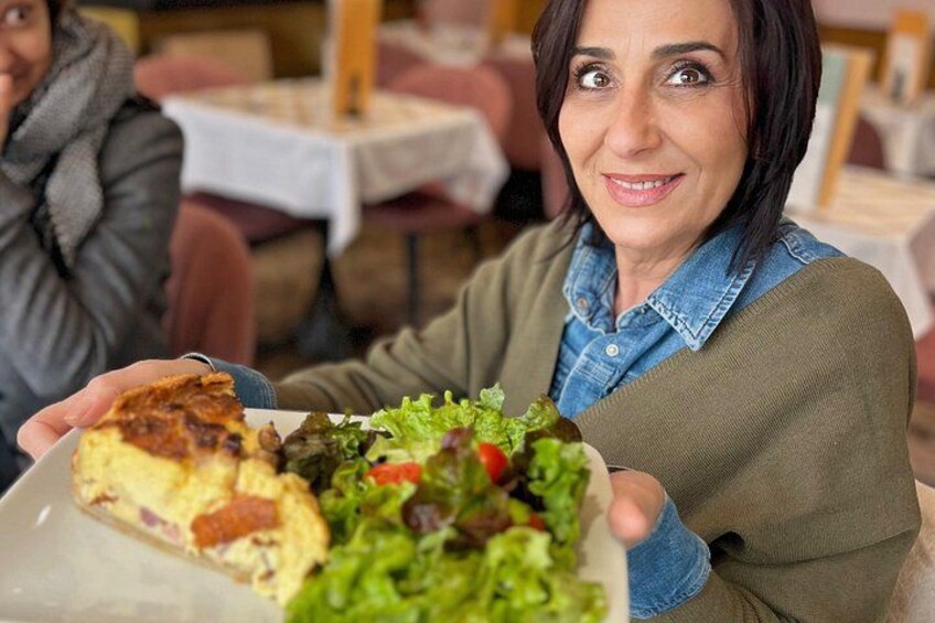 A person holding a plate with a slice of quiche and a salad. 3