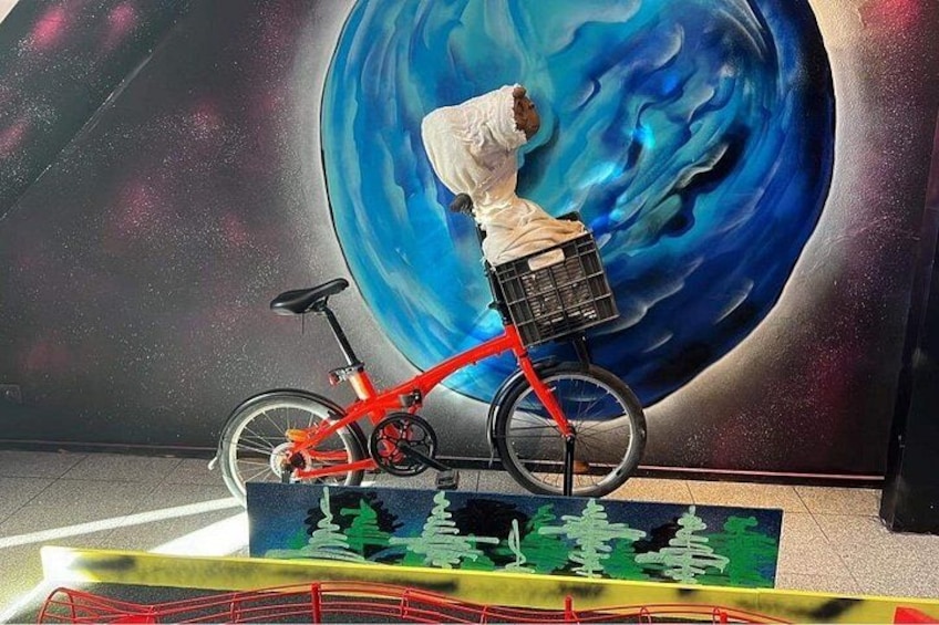 Un vélo rouge avec un panier, une personne portant une veste blanche et une grande fresque représentant une planète. 5