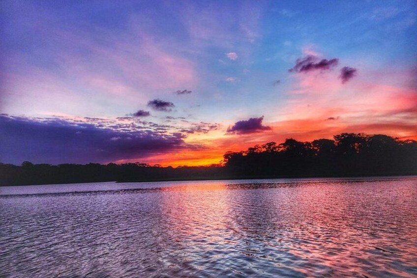 A sunset over a body of water with a silhouette of trees in the background. 2