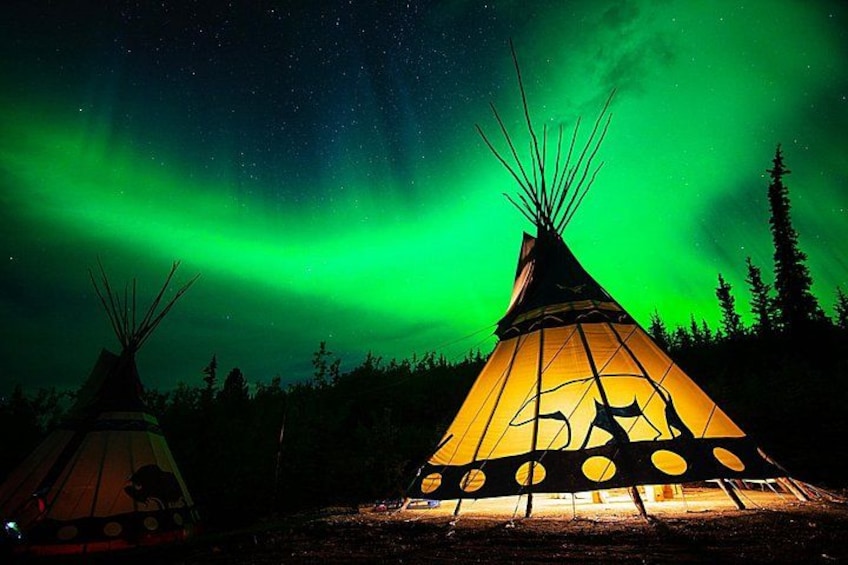Two tipi tents illuminated by a campfire, set against a night sky with the aurora borealis. 1