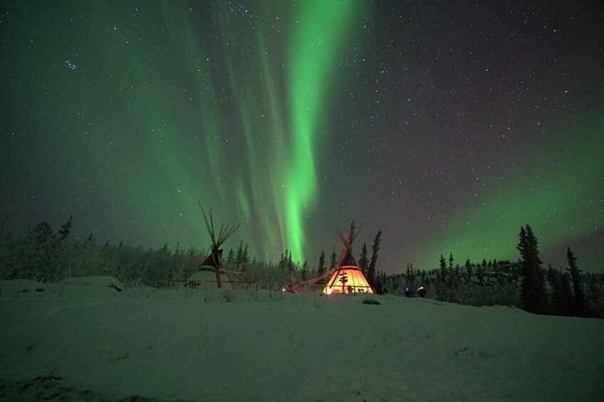 Paisaje nevado con un tipi y una cabaña bajo un cielo nocturno con auroras boreales verdes. 4
