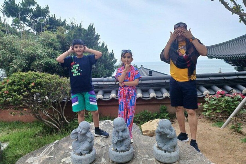 Three people standing in front of a traditional building with a tiled roof, surrounded by greenery and stone statues. 5