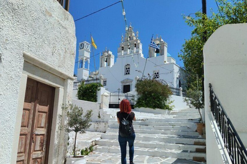 Una persona sube por una escalera de piedra blanca hacia una iglesia blanca con cúpulas azules y una torre del reloj. 2