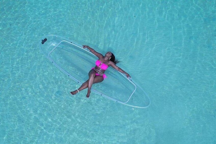 En person ligger på en klarblå pool med en genomskinlig bräda, och bär en rosa baddräkt. 1