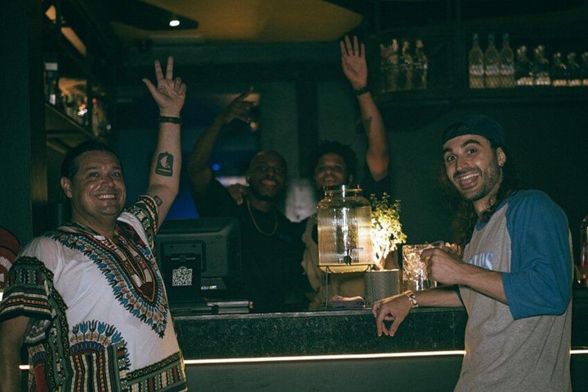 A bar with a counter, bottles, and a person holding a glass. 3