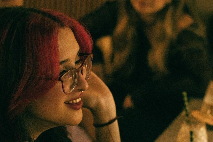 A person with red hair and glasses, sitting at a table with a drink. 2