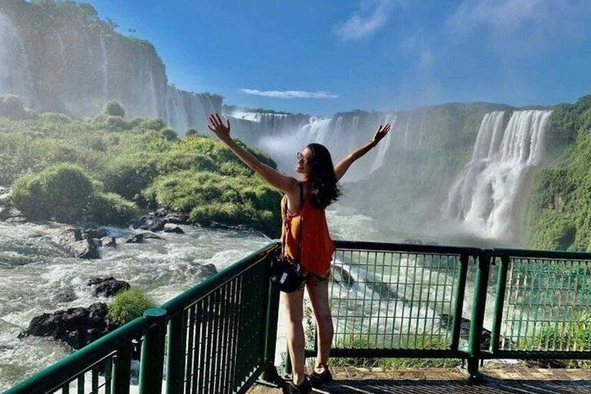 A person standing on a bridge with arms outstretched, overlooking a waterfall. 5