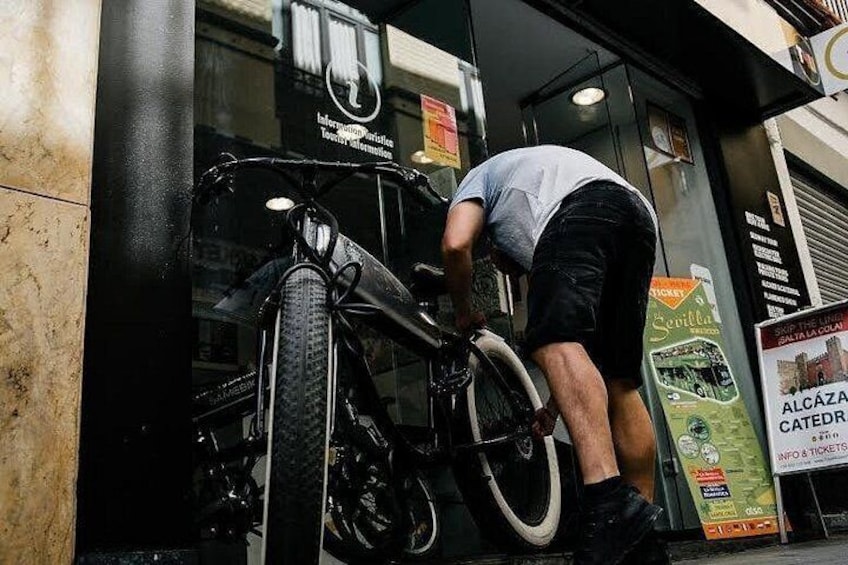 A person leaning over a bicycle parked in front of a building with a sign that reads 'Alcázar Catedrático.' 2