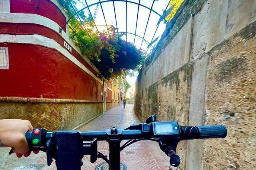 A bicycle with a hand on the handlebar, a red wall, and a person walking in the background. 4