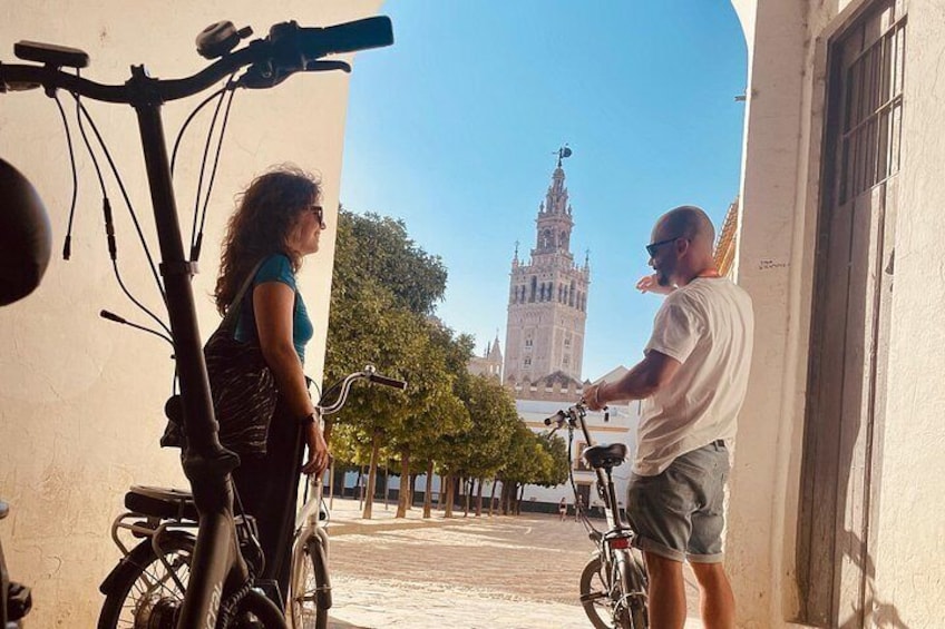 Una persona in bicicletta, un'altra con una macchina fotografica e un edificio storico sullo sfondo. 1