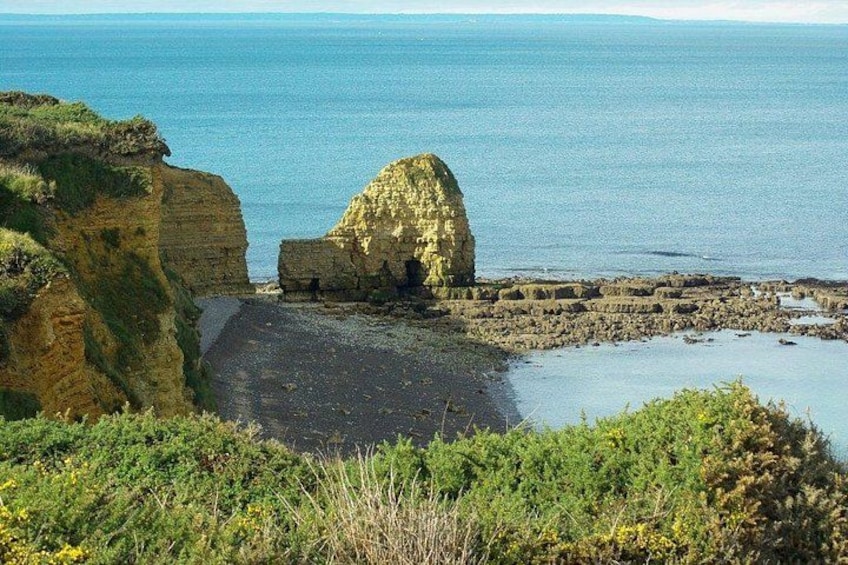 Eine Küstenlandschaft mit Klippen, einem Strand und einer großen Felsformation. 2