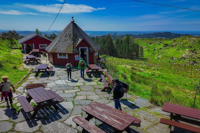 A stone patio with picnic tables, a red-roofed building, and a grassy hillside. 4