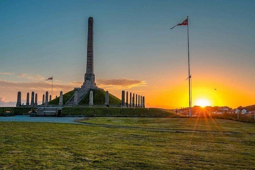 A monument with a tall obelisk, a flagpole, and a grassy field at sunset. 2