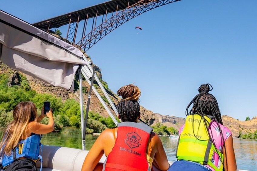 Three people on a boat, wearing life jackets, with a bridge and a canyon in the background. 1