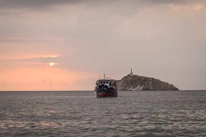 Un bateau sur une étendue d’eau calme, avec une île rocheuse et un phare en arrière-plan. 5