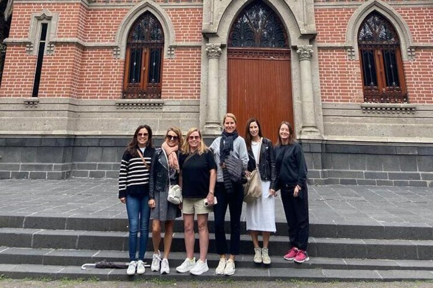 A group of people standing on steps in front of a brick building with arched windows and a wooden door. 5