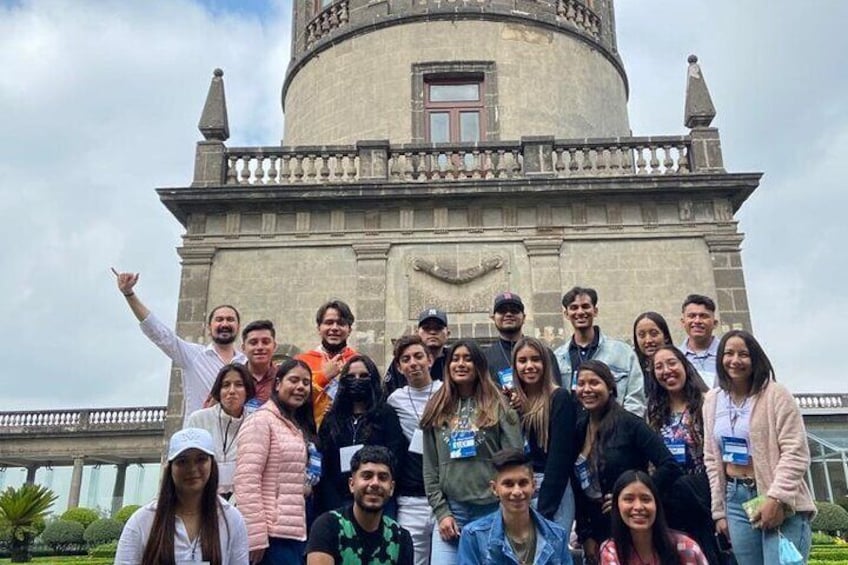 A group of people posing in front of a historic tower with a clock and a balcony. 3