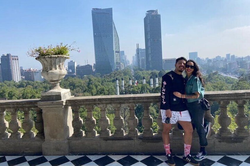 A couple standing on a balcony with a cityscape in the background. 4