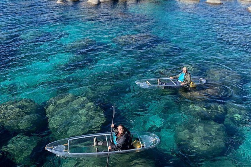 Dos personas kayakendo en aguas azules y transparentes, con rocas visibles bajo el agua. 2