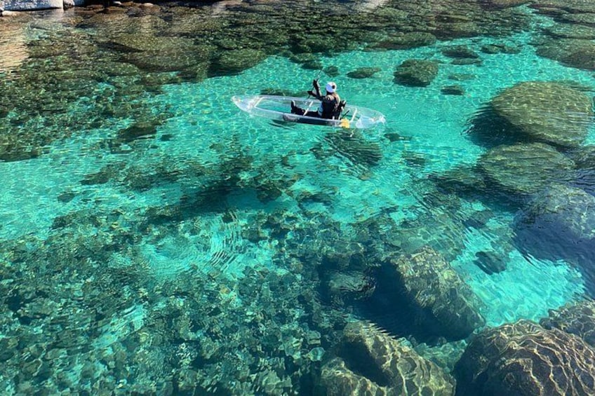 A person kayaking on clear turquoise water with visible underwater rocks. 2