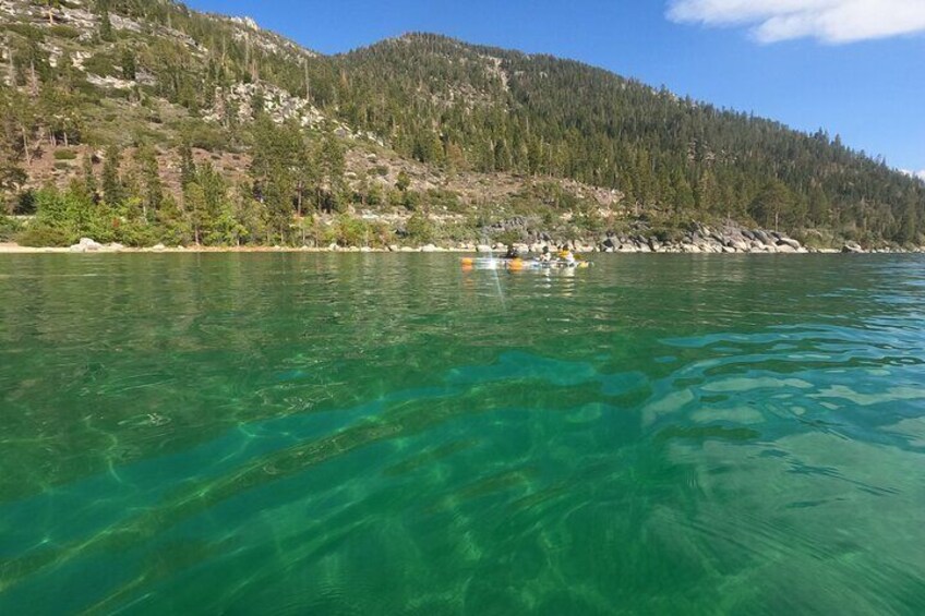 Un lago transparente con un barco a lo lejos y una montaña boscosa al fondo. 3