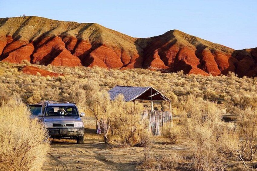 A vehicle on a dirt road, a wooden structure, and red rock formations. 1