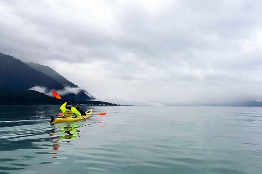 A kayaker in a yellow kayak on calm water with mountains in the background. 4