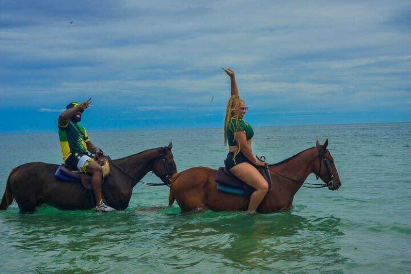 Two people riding horses in shallow water near a body of water. 1